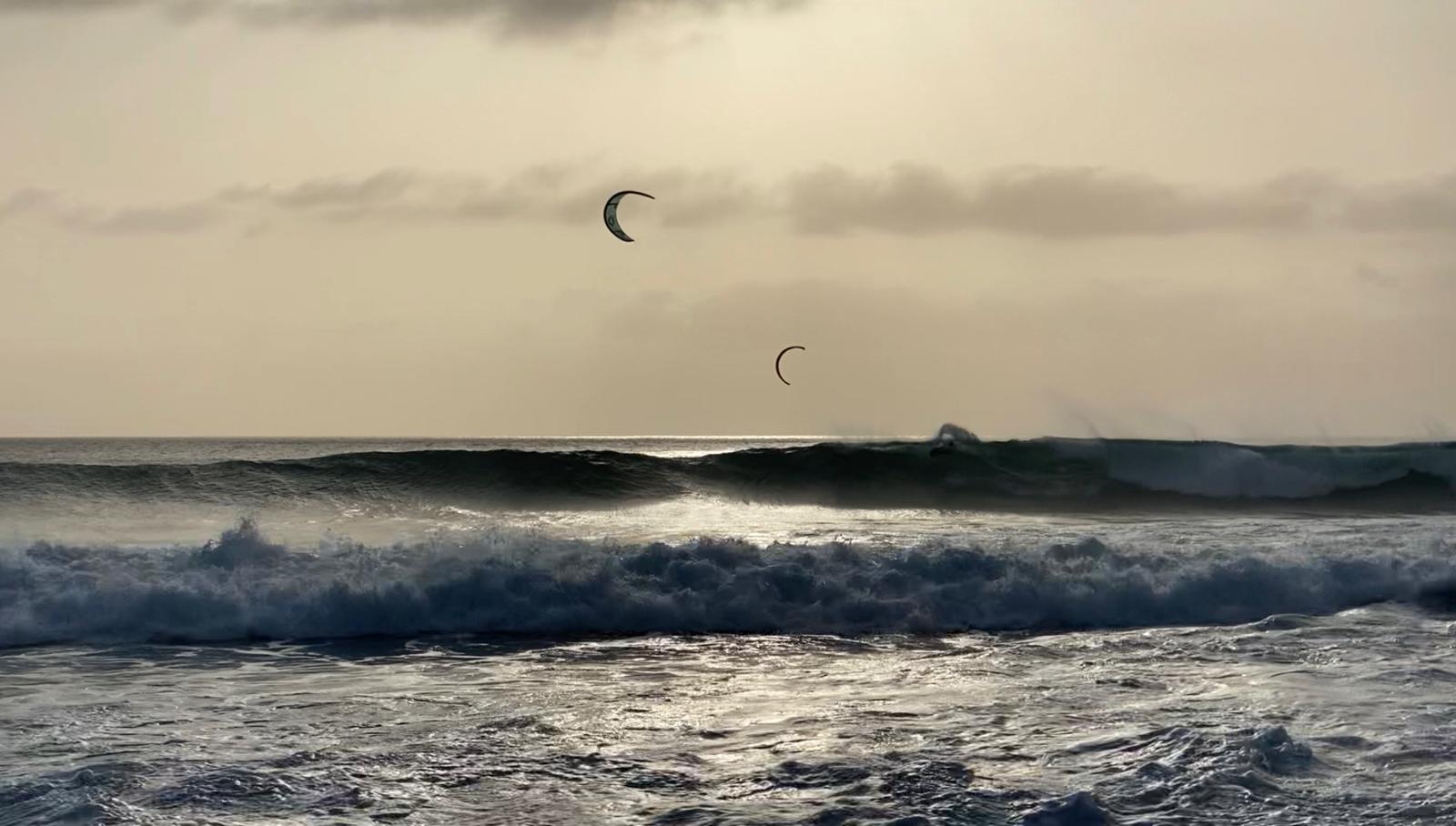 Two kitesurfers in sunset colors riding big waves at Ponta Preta on Sal Cabo Verde
