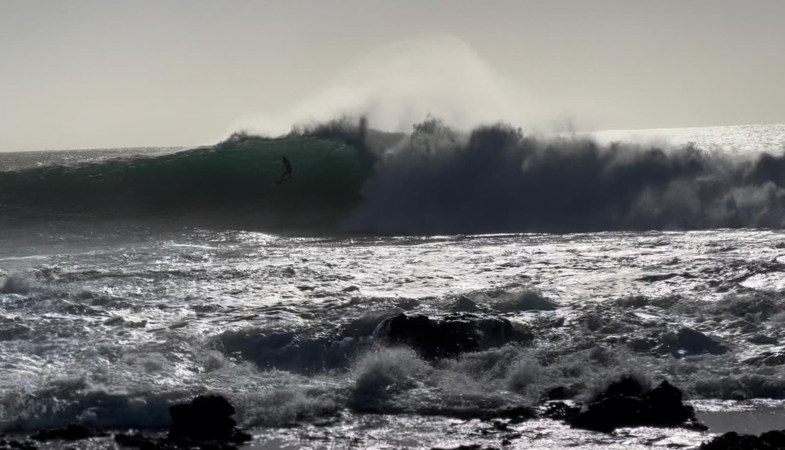Surfer riding a wave off the coast of Palmeira, Sal, with a sailing boat in the background on the Atlantic Ocean.
